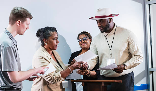 A mature black man giving a seminar, standing at the front of a meeting room by a lectern, handing out information.